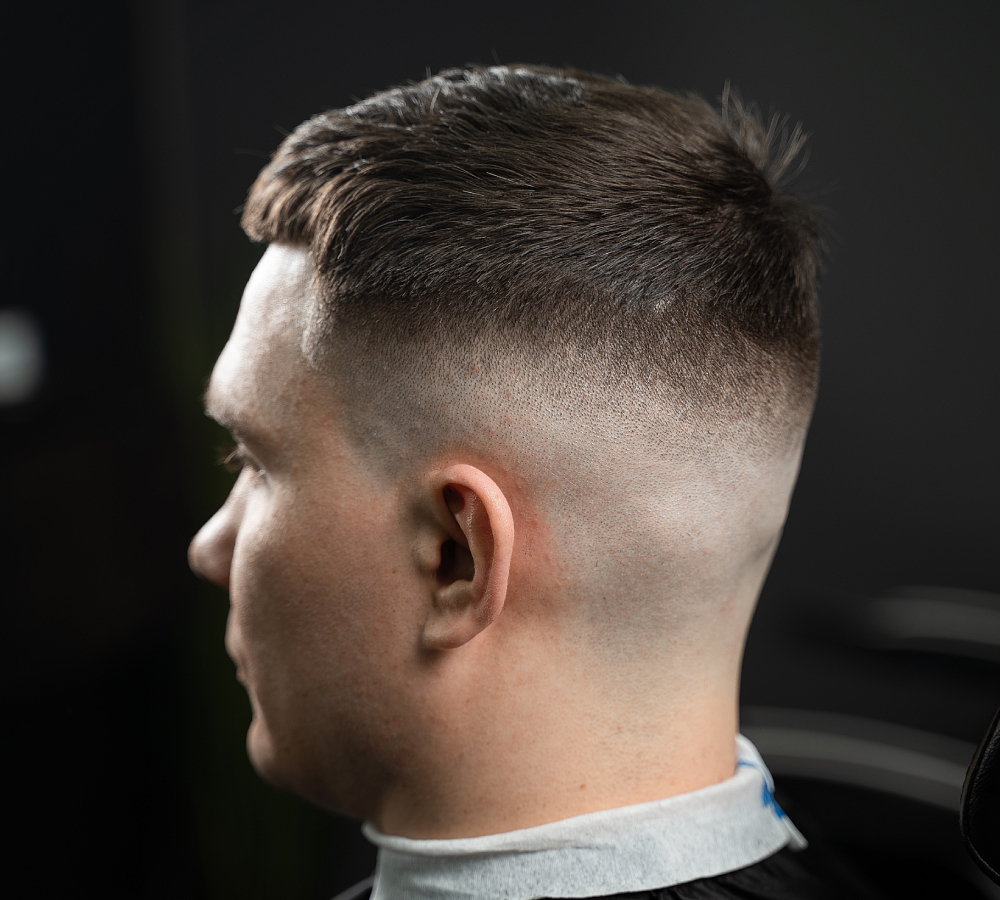 Close-up profile of a high skin fade haircut with a short, textured fringe on a male client in a barber shop.